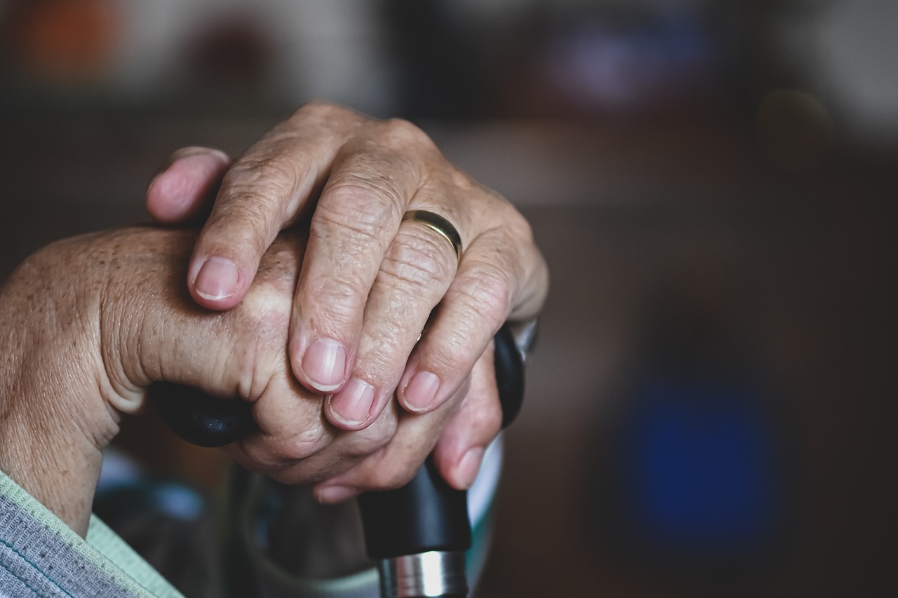 Elderly hands crossed over a walking cane.