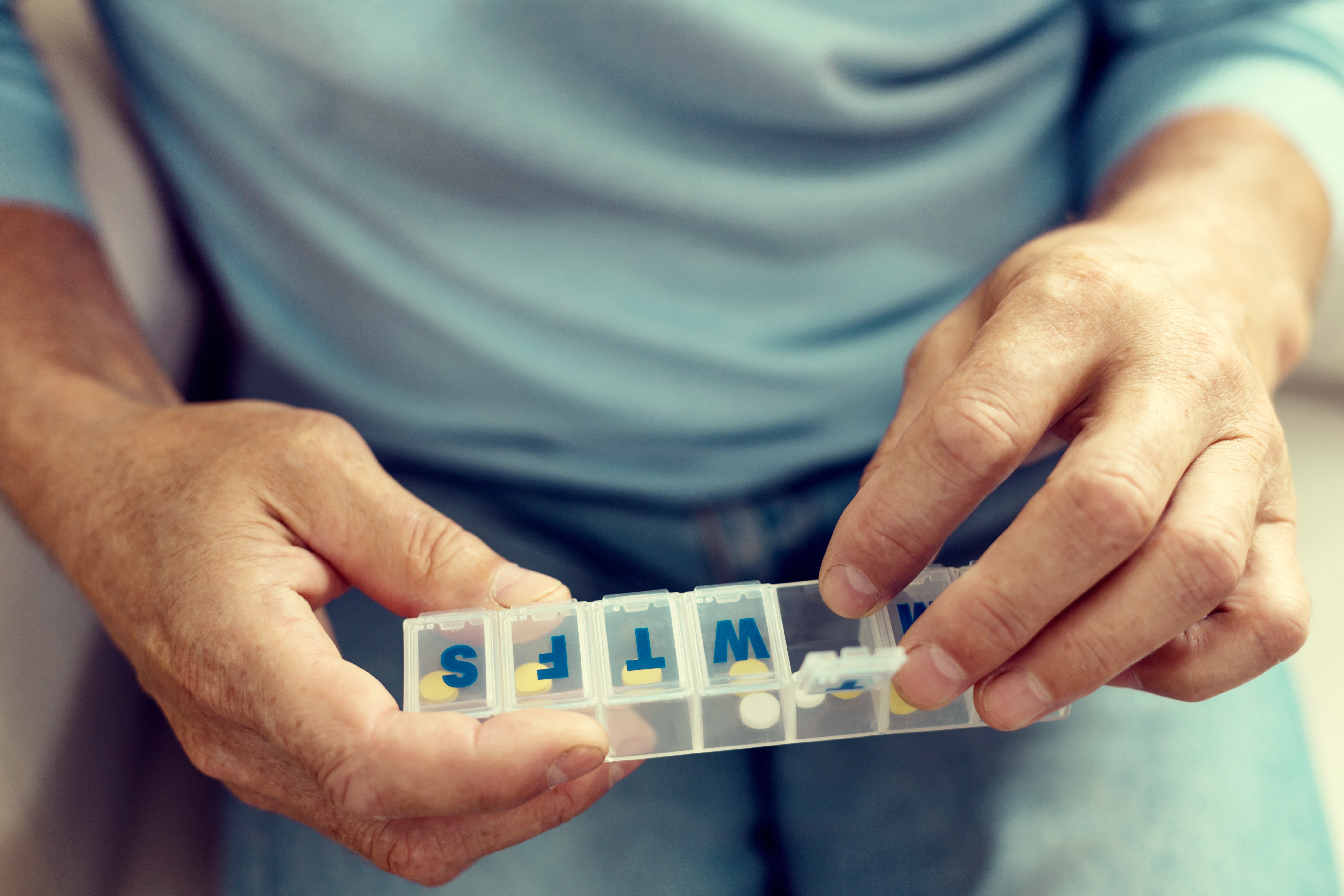 Weekly pill dispenser for elderly parents – older adult using a daily pill organiser with labelled compartments to manage medication safely and independently at home.